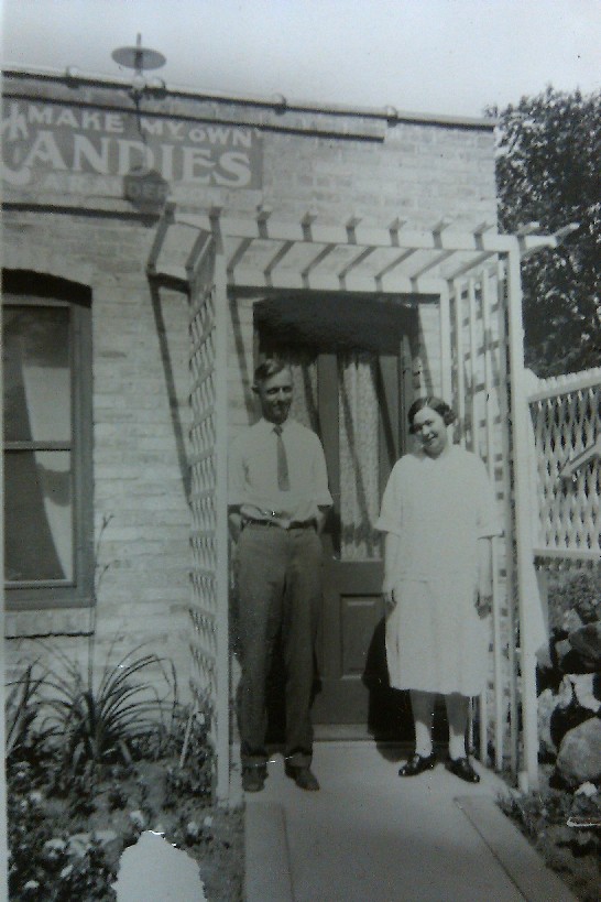 Arthur and Gertrude (the founders of Anderson's Candy Shop) stand outside of their business. The sign above their heads reads: I MAKE MY OWN CANDIES